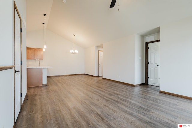 unfurnished living room featuring wood-type flooring, sink, ceiling fan with notable chandelier, and high vaulted ceiling