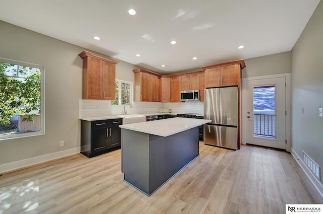 kitchen featuring sink, appliances with stainless steel finishes, backsplash, a center island, and light wood-type flooring