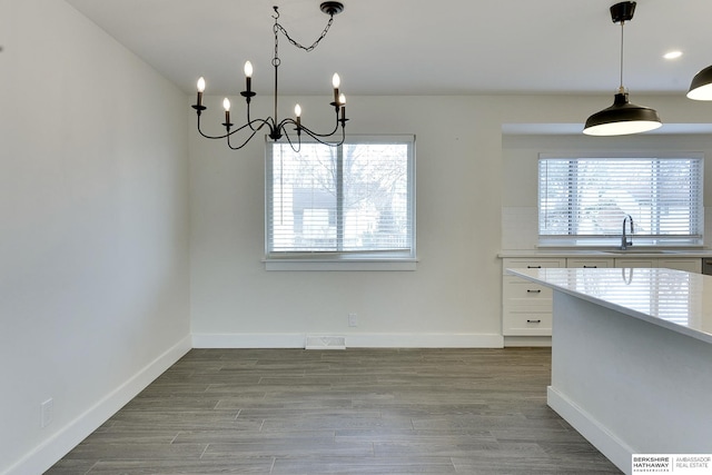 unfurnished dining area featuring an inviting chandelier, sink, a healthy amount of sunlight, and light wood-type flooring