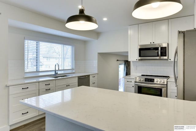 kitchen with appliances with stainless steel finishes, decorative light fixtures, white cabinetry, sink, and light stone counters