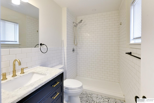 bathroom with vanity, a tile shower, tile walls, and toilet