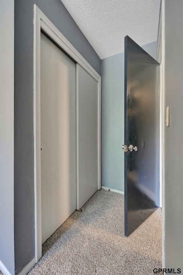 hallway featuring light colored carpet and a textured ceiling