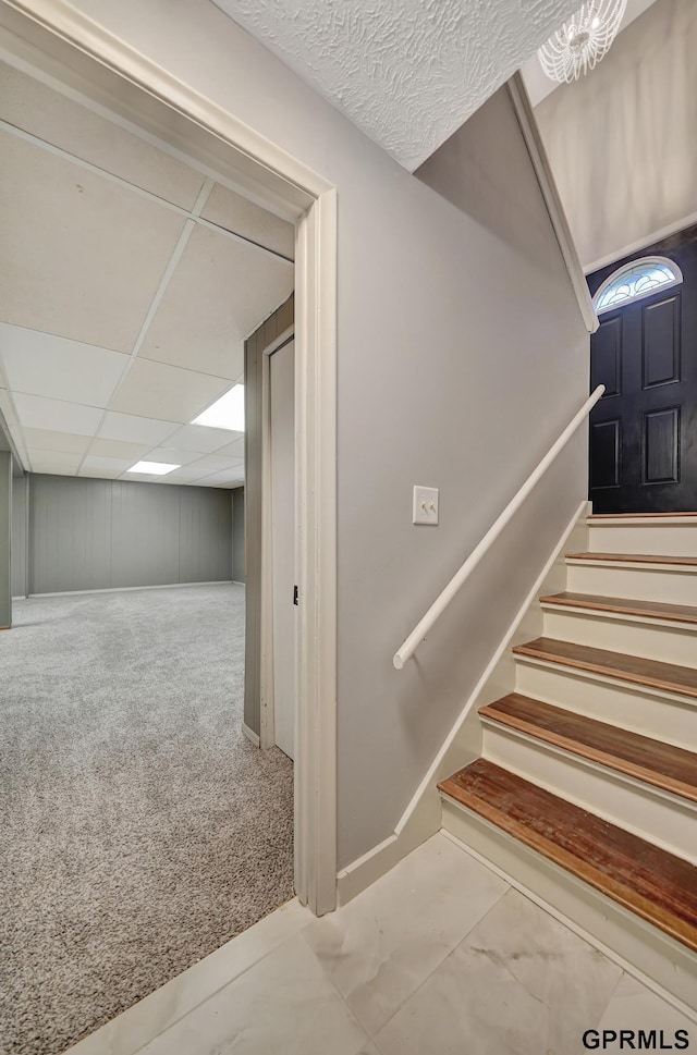 stairway featuring carpet flooring and a drop ceiling