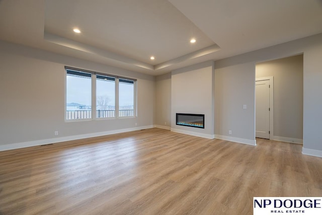 unfurnished living room featuring a raised ceiling and light hardwood / wood-style floors