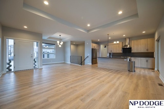 unfurnished living room featuring a chandelier, light wood-type flooring, and a tray ceiling