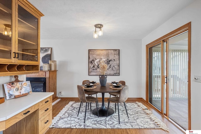 dining space featuring a glass covered fireplace, a textured ceiling, baseboards, and light wood-style floors