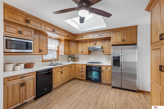 kitchen with under cabinet range hood, light countertops, light wood-style flooring, black appliances, and a sink