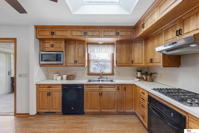 kitchen with black appliances, light countertops, under cabinet range hood, and a sink