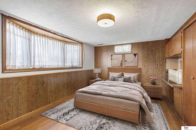 bedroom featuring a textured ceiling, wood finished floors, wainscoting, and wood walls