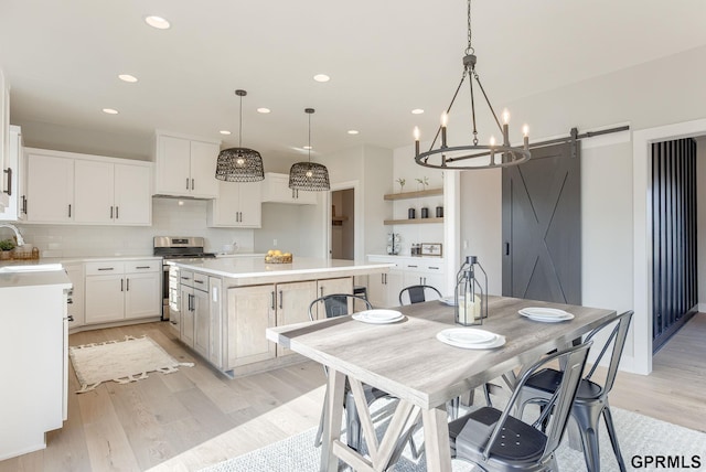 kitchen with sink, a center island, stainless steel stove, a barn door, and white cabinets