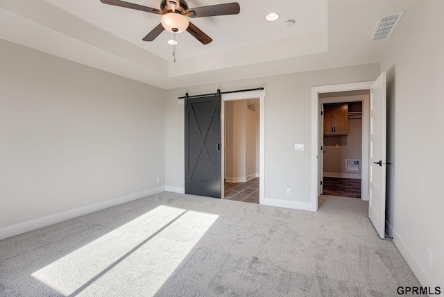 unfurnished bedroom featuring light carpet, a tray ceiling, a barn door, and a spacious closet