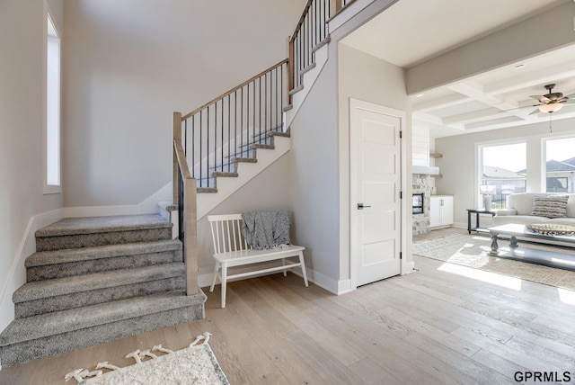 stairway with coffered ceiling, a stone fireplace, wood-type flooring, ceiling fan, and beam ceiling