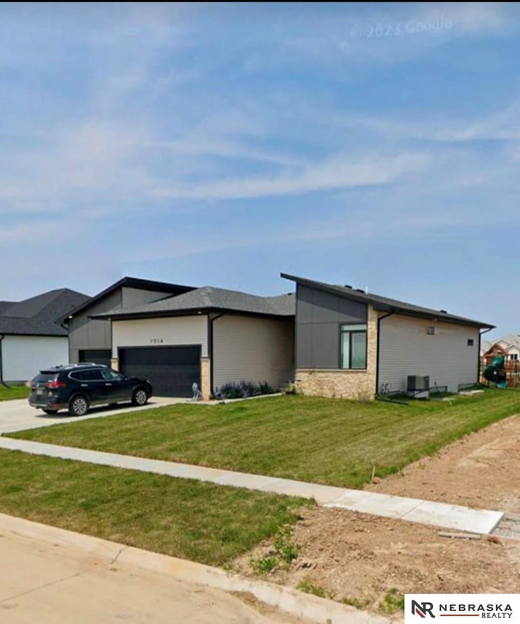 view of front of home with concrete driveway, central air condition unit, a garage, and a front lawn