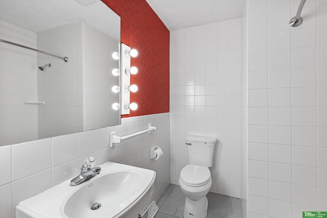 bathroom featuring sink, tile patterned flooring, tile walls, tiled shower, and toilet