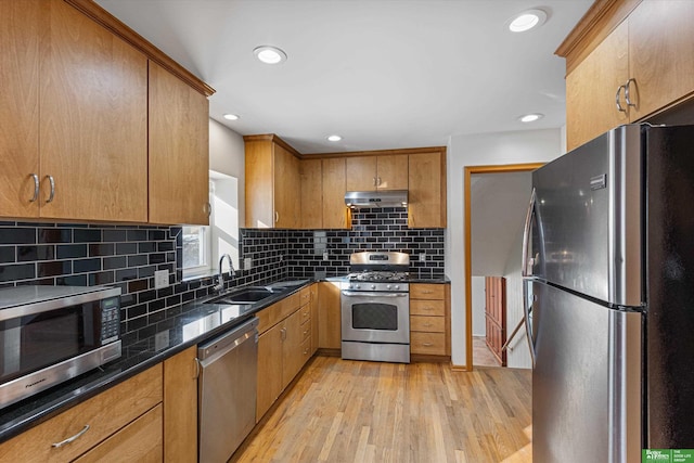 kitchen with sink, light hardwood / wood-style flooring, dark stone countertops, stainless steel appliances, and backsplash