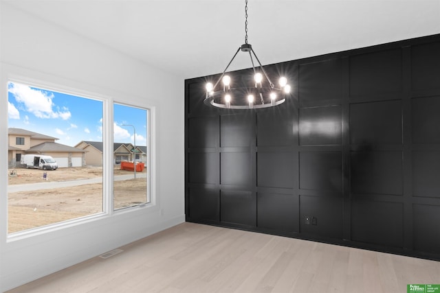 unfurnished dining area with a notable chandelier and light wood-type flooring