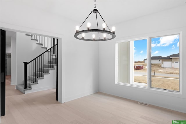 unfurnished dining area featuring an inviting chandelier and light hardwood / wood-style flooring