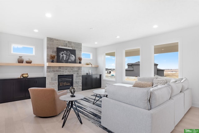 living room featuring a stone fireplace, a healthy amount of sunlight, and light wood-type flooring