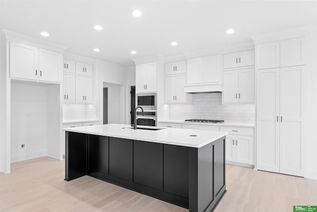 kitchen with sink, stainless steel appliances, white cabinets, a center island with sink, and light wood-type flooring