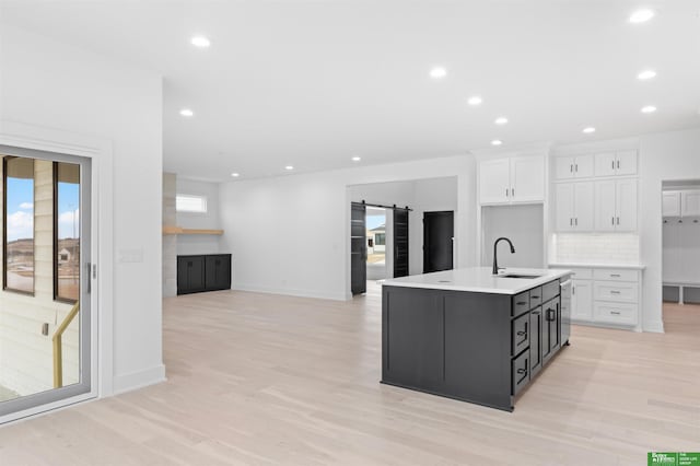 kitchen featuring a barn door, a kitchen island with sink, light hardwood / wood-style flooring, and white cabinets