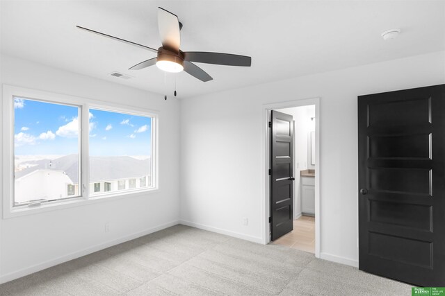 unfurnished bedroom featuring light colored carpet, ceiling fan, and ensuite bathroom