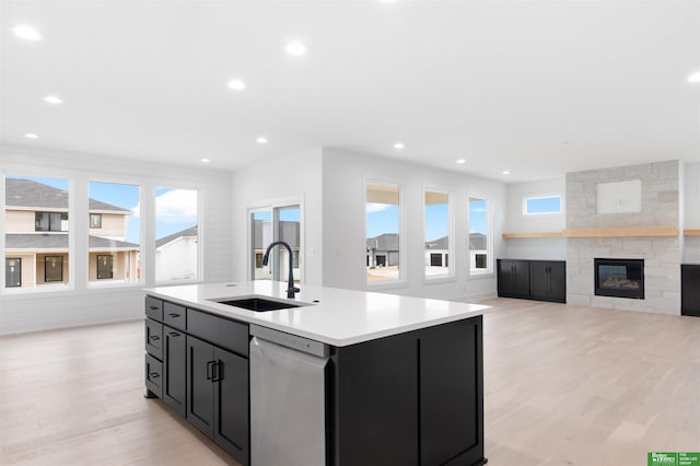 kitchen featuring a stone fireplace, sink, a center island with sink, light wood-type flooring, and dishwasher