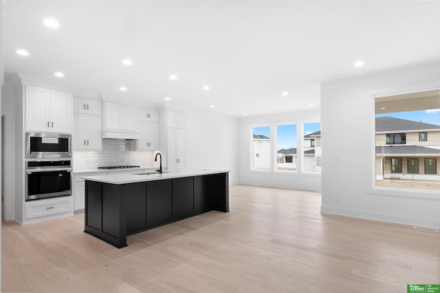 kitchen with tasteful backsplash, an island with sink, sink, white cabinets, and stainless steel appliances