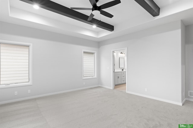 unfurnished bedroom with a tray ceiling, connected bathroom, beam ceiling, and light carpet