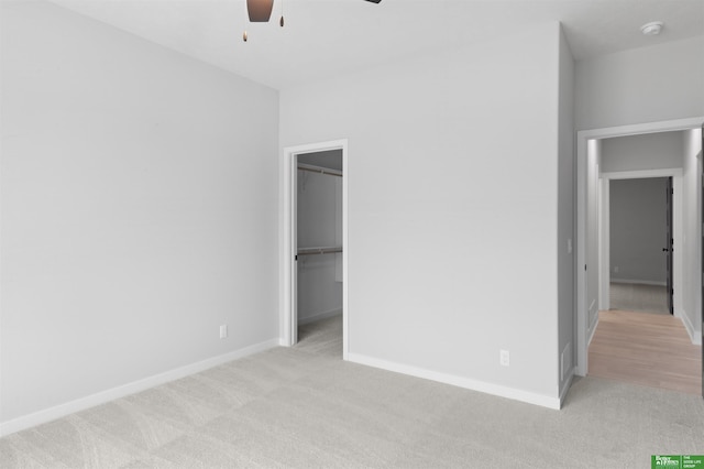 unfurnished bedroom with ceiling fan, a walk in closet, a closet, and light carpet