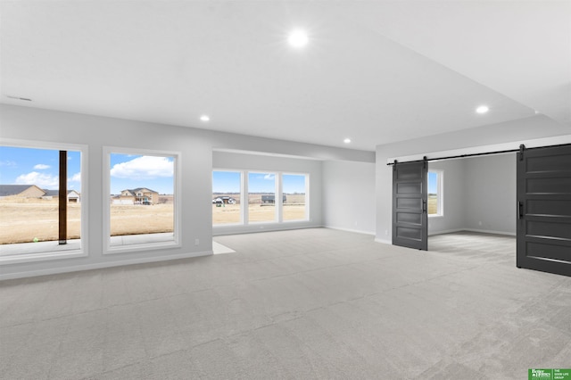 unfurnished living room featuring light colored carpet, a healthy amount of sunlight, and a barn door