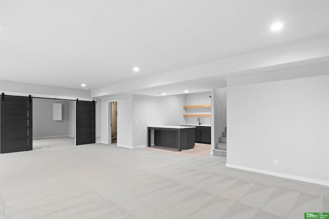 basement featuring light colored carpet, a barn door, and bar area