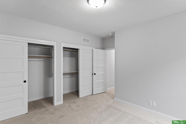 unfurnished bedroom with multiple closets and light colored carpet