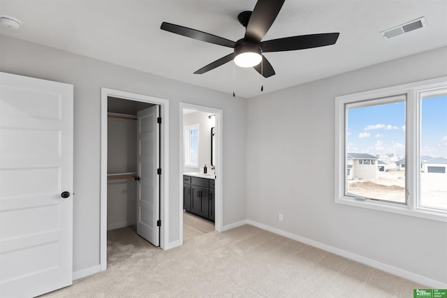 unfurnished bedroom featuring sink, ensuite bath, a walk in closet, light colored carpet, and a closet