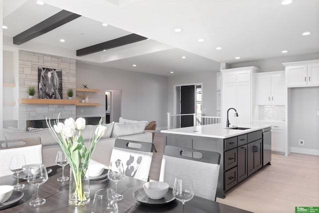 kitchen featuring dishwasher, white cabinetry, sink, decorative backsplash, and a center island with sink