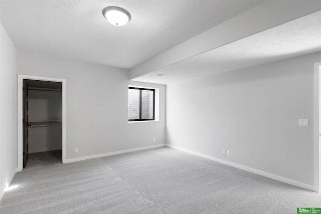 unfurnished bedroom with a walk in closet, a closet, light carpet, and a textured ceiling