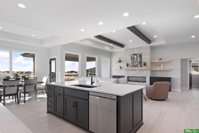 kitchen with stainless steel dishwasher, sink, an island with sink, and light wood-type flooring