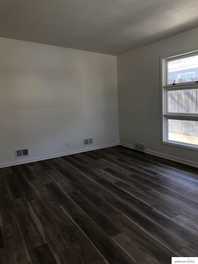 empty room with dark wood-style floors, baseboards, and visible vents