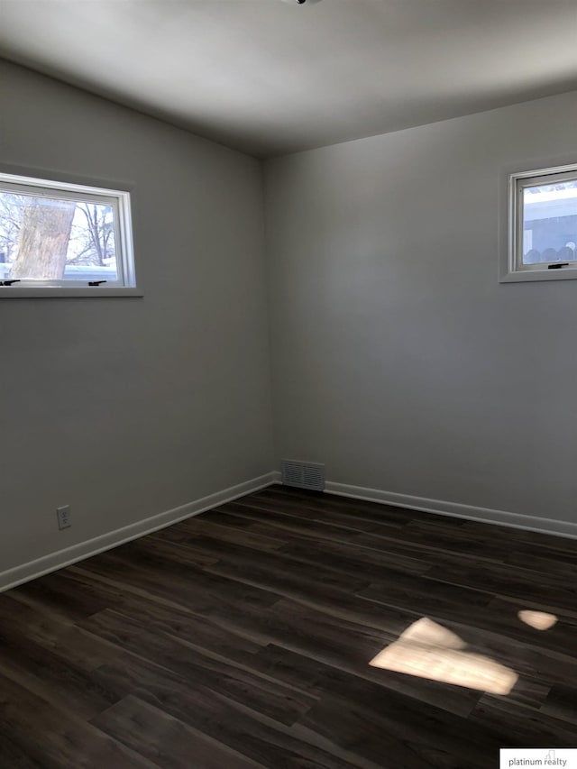 spare room featuring dark wood-style floors, visible vents, and baseboards