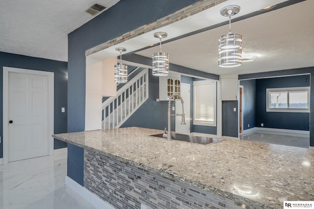 kitchen featuring sink, light stone countertops, hanging light fixtures, and a textured ceiling