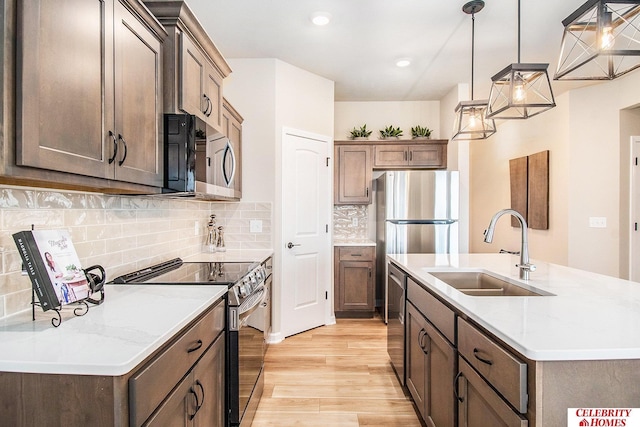 kitchen featuring sink, hanging light fixtures, stainless steel appliances, a center island with sink, and light hardwood / wood-style flooring