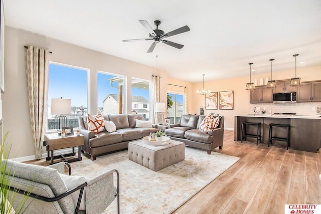 living room with ceiling fan with notable chandelier and light hardwood / wood-style flooring