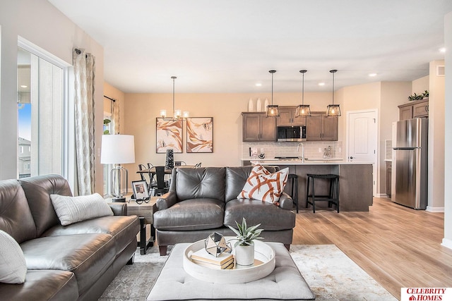 living room featuring an inviting chandelier, sink, and light wood-type flooring