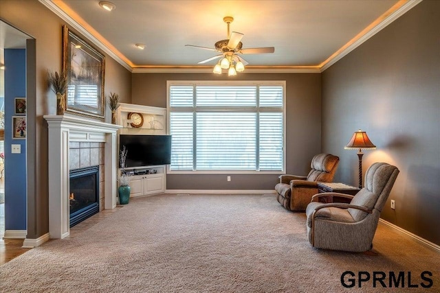 living area featuring a tiled fireplace, crown molding, ceiling fan, and carpet flooring