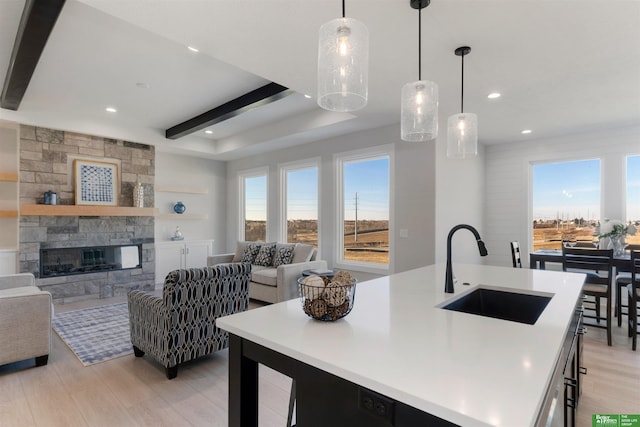 kitchen featuring a stone fireplace, pendant lighting, sink, a kitchen island with sink, and beam ceiling