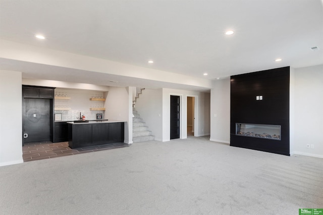 unfurnished living room with bar, a fireplace, and dark colored carpet