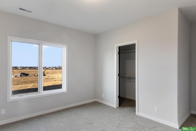 unfurnished bedroom featuring a walk in closet, light colored carpet, and a closet