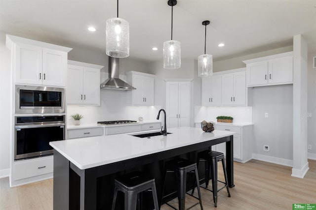 kitchen featuring sink, hanging light fixtures, stainless steel appliances, an island with sink, and white cabinets