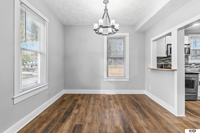 unfurnished dining area featuring an inviting chandelier, dark hardwood / wood-style flooring, a textured ceiling, and a wealth of natural light