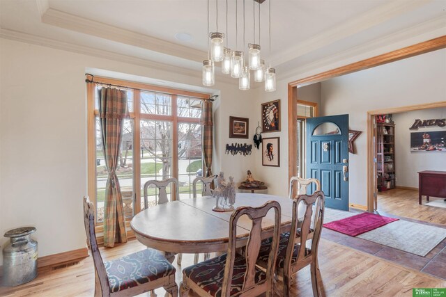 dining space with crown molding, a raised ceiling, and light hardwood / wood-style floors