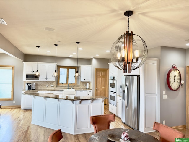 kitchen with appliances with stainless steel finishes, pendant lighting, white cabinets, and dark stone counters